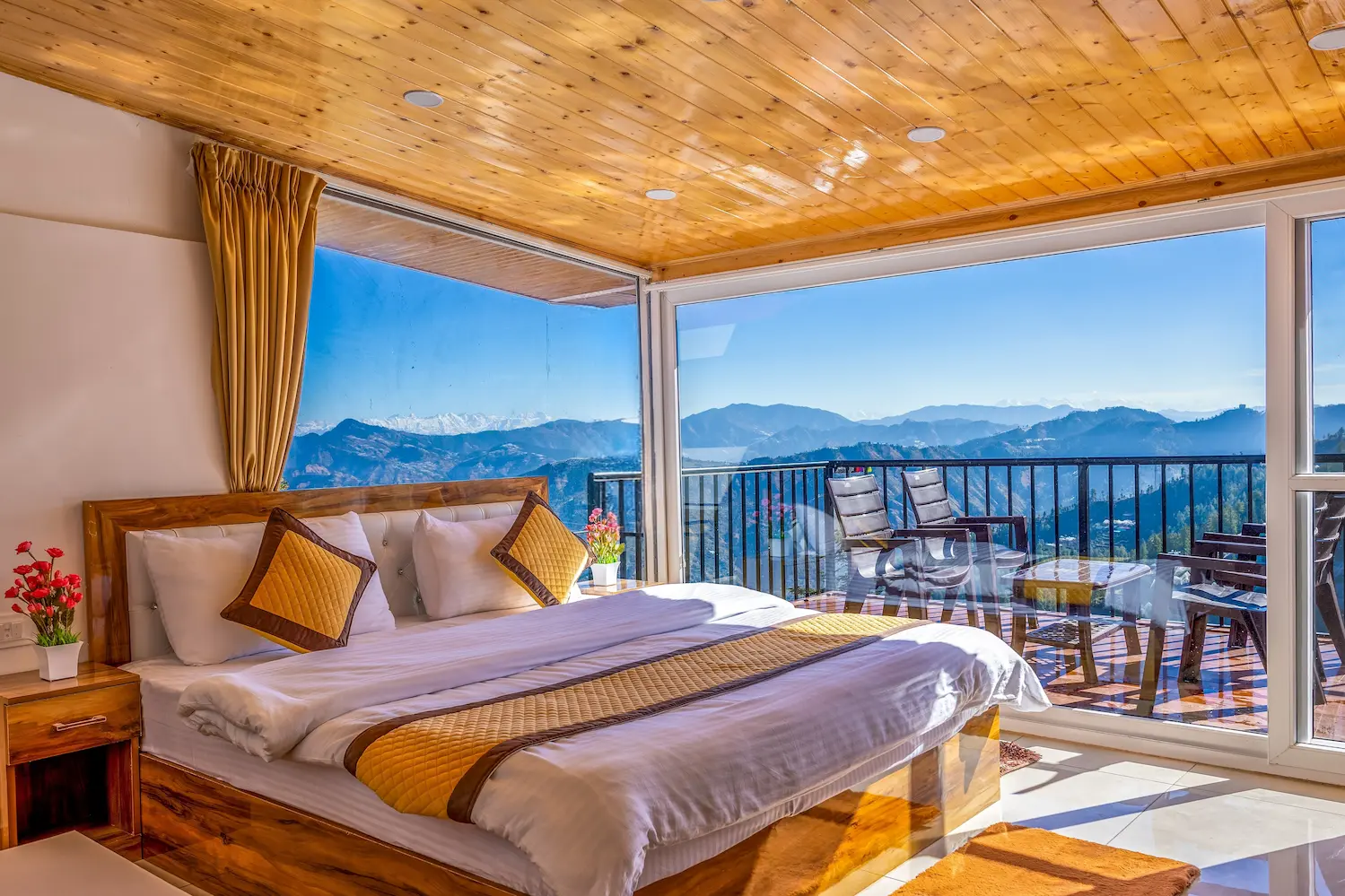 Attic bedroom under a pine ceiling, its glass wall opening to snow-capped Himalayan peaks