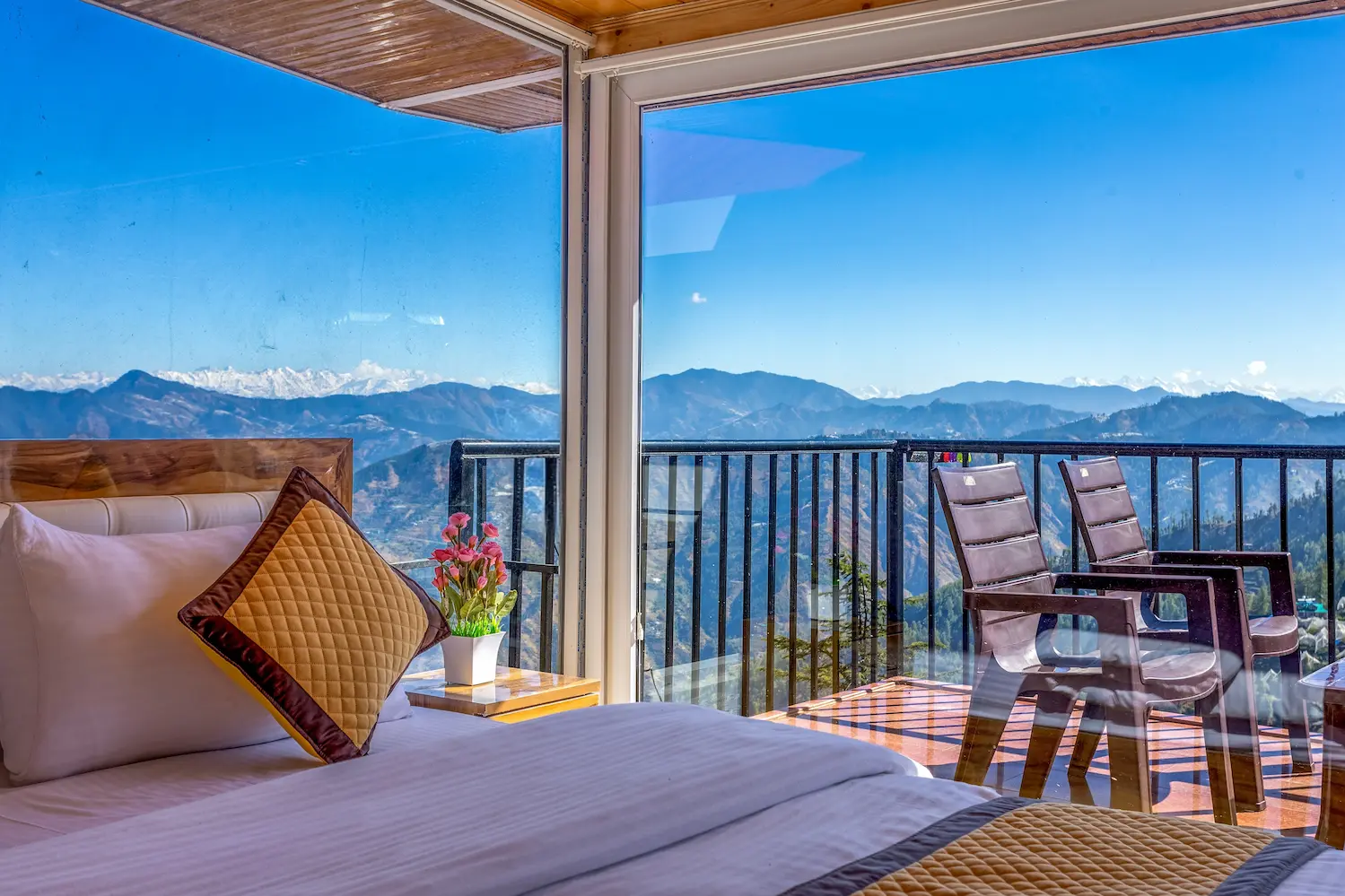 Attic suite bed set against glass, with balcony chairs and snow peaks beyond
