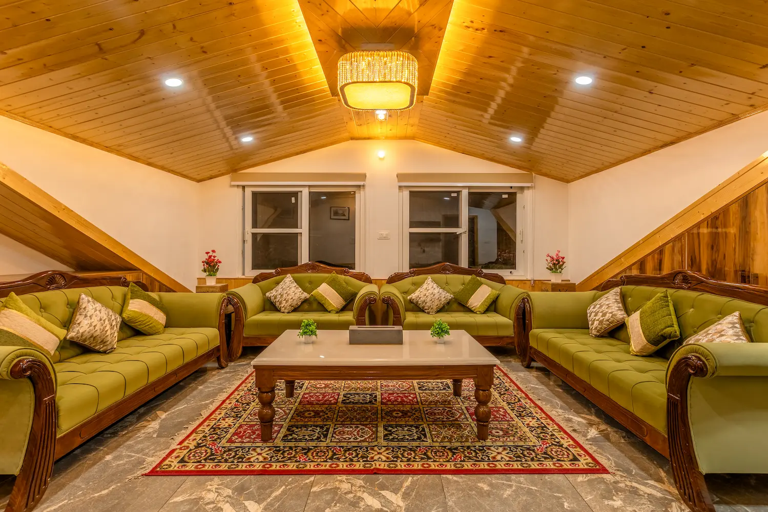 Attic living room with four green sofas facing each other under a vaulted pine ceiling